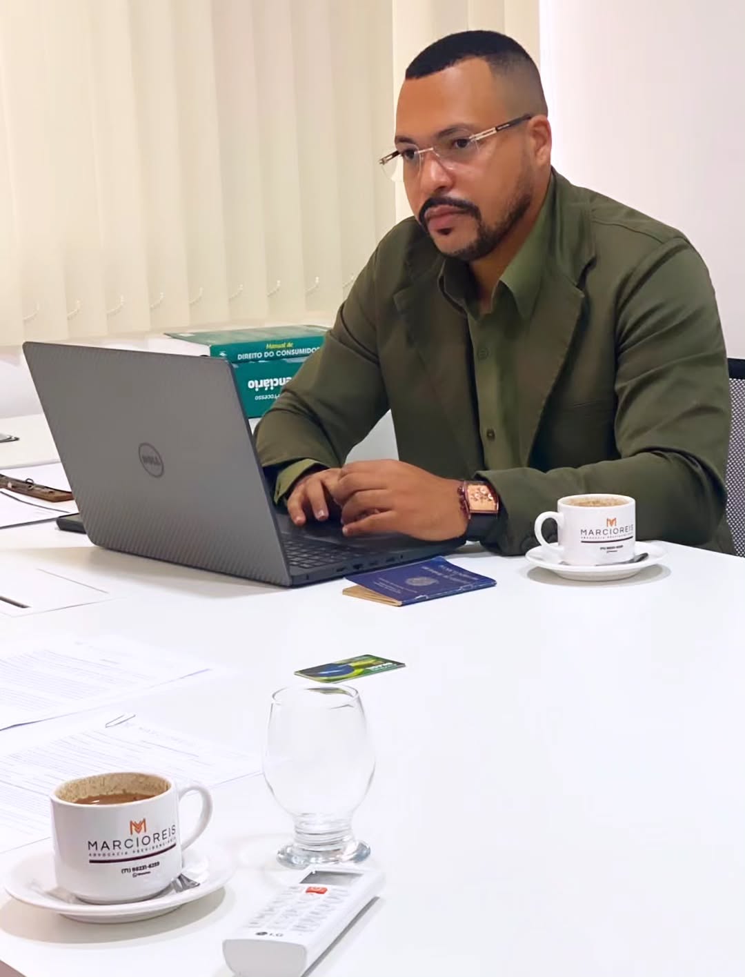 Marcio Reis no escritório, ao notebook, com uma carteira de trabalho sobre a mesa